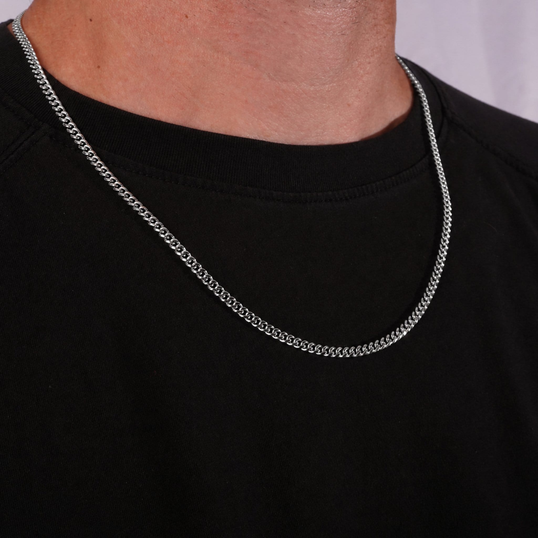 Silver cuban chain necklace on a person wearing a black shirt against a gray background