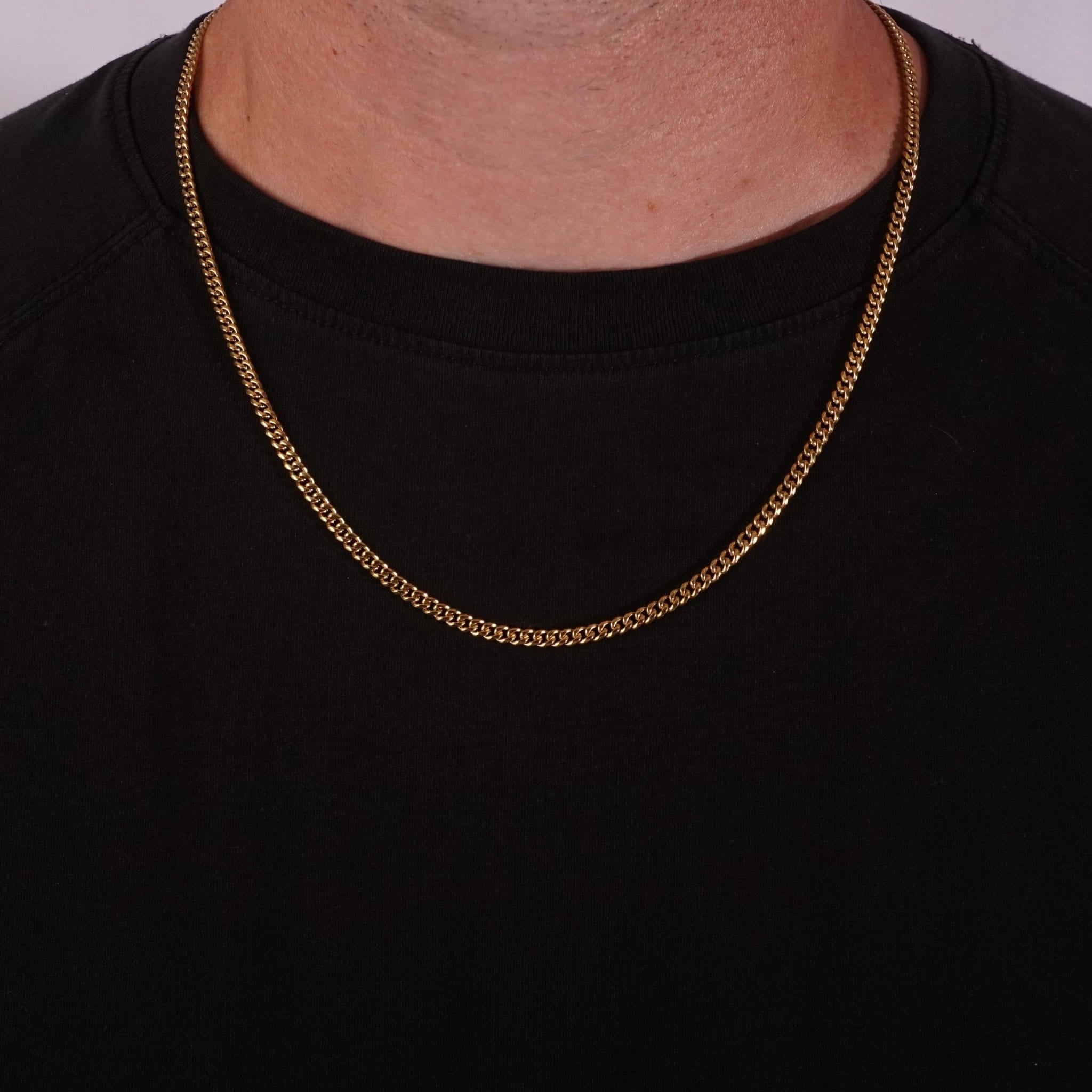 Gold cuban chain necklace on a black shirt against a white background