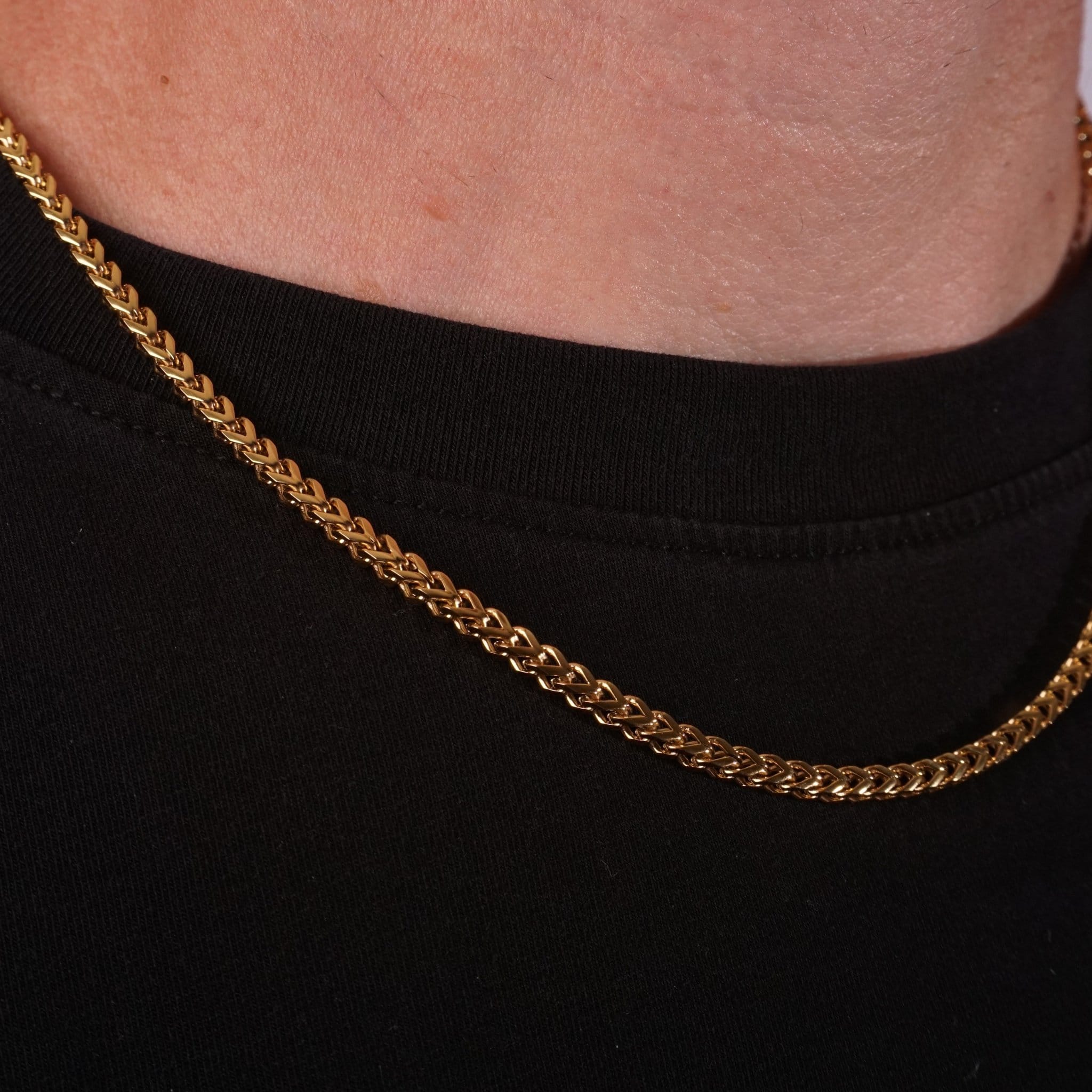 Closeup of a gold franco chain around a person's neck against a black background