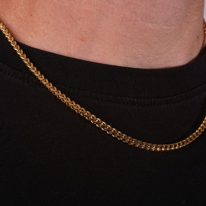 Closeup of a gold franco chain around a person's neck against a black background
