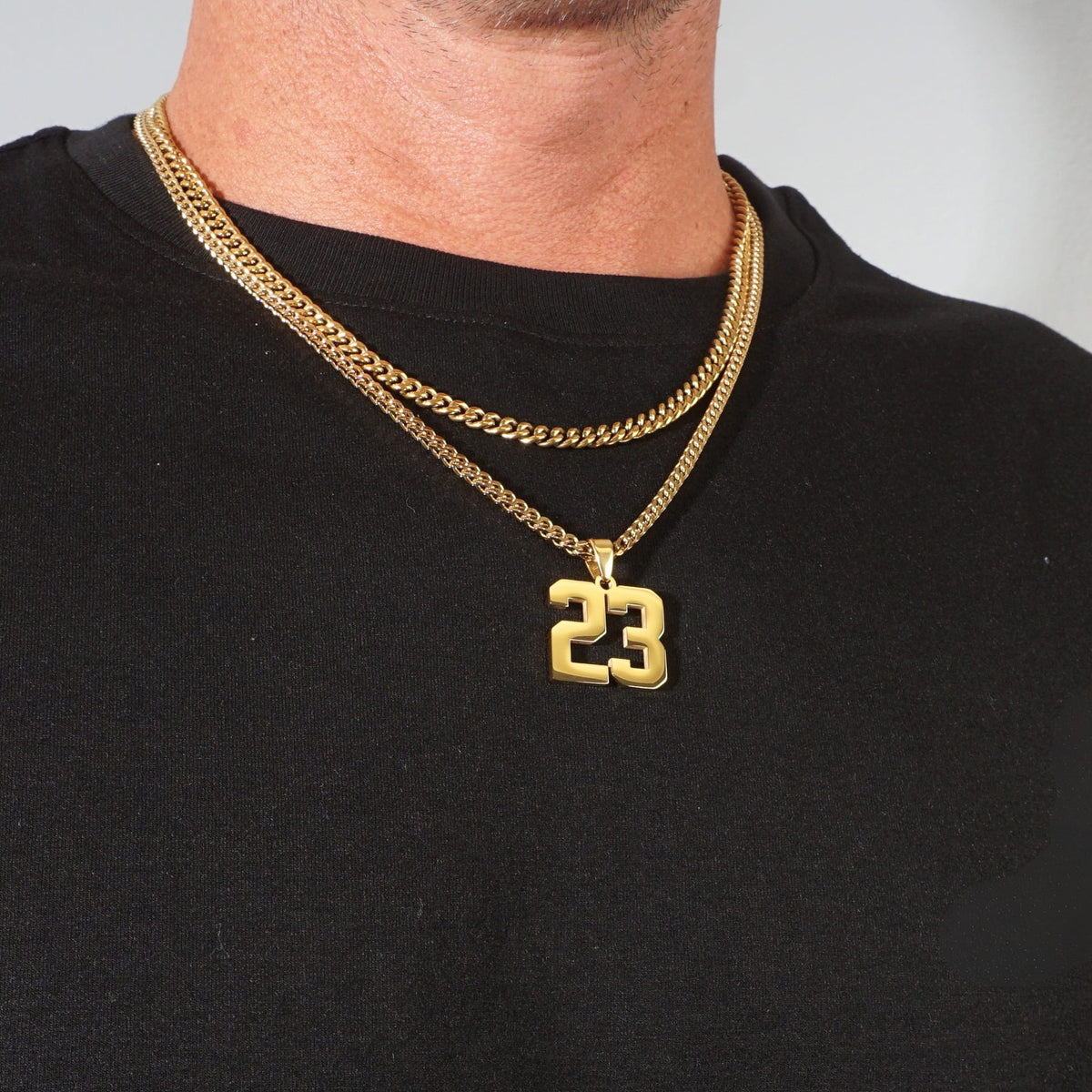 A close-up of a man's neck and chest wearing the franco and cuban stack with a '23' number pendant, styled with a black t-shirt.