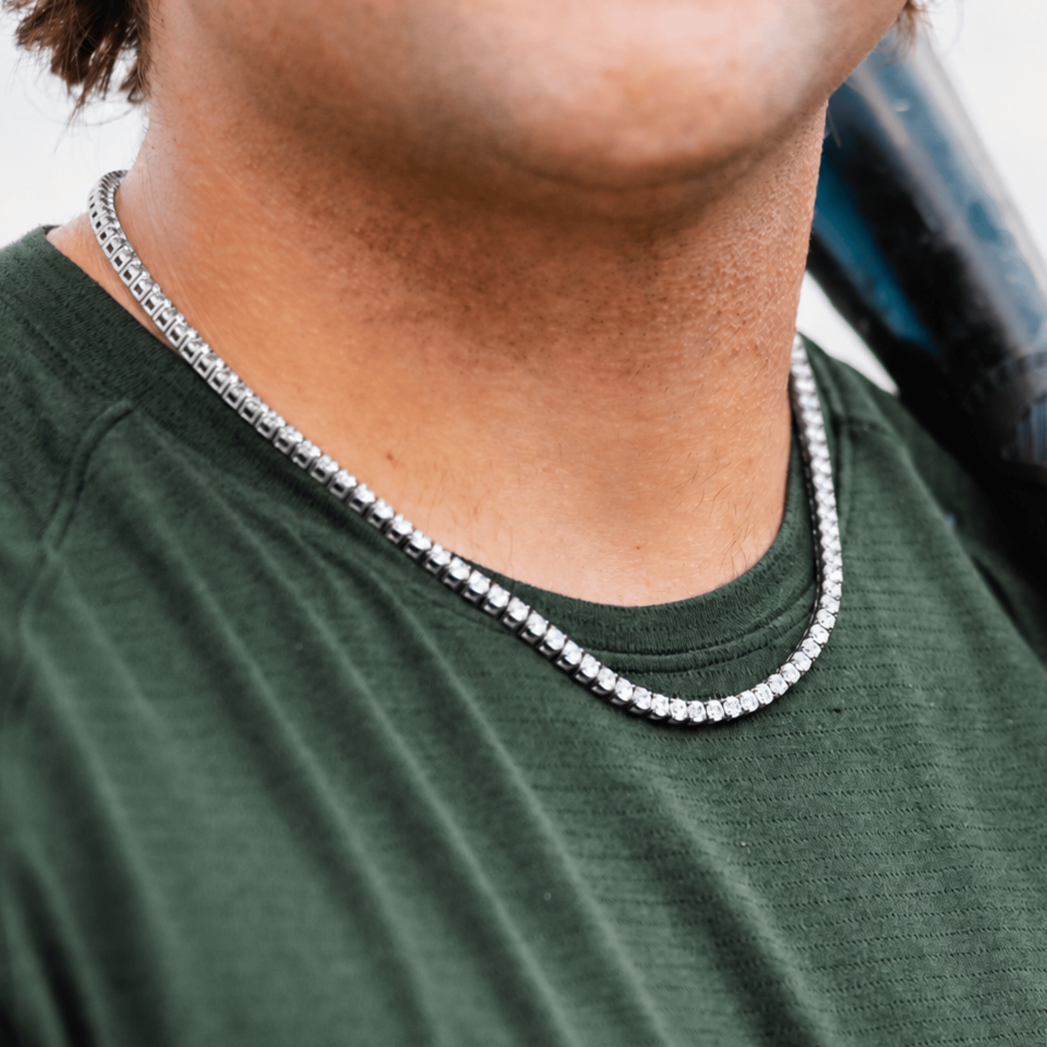 A close-up of a person wearing a silver tennis chain with a textured link design, paired with a dark green t-shirt.